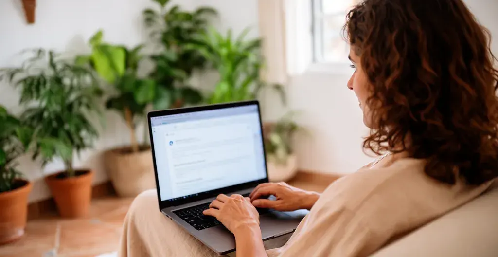 Mujer española consultando datos inmobiliarios en portátil en salón mediterráneo luminoso